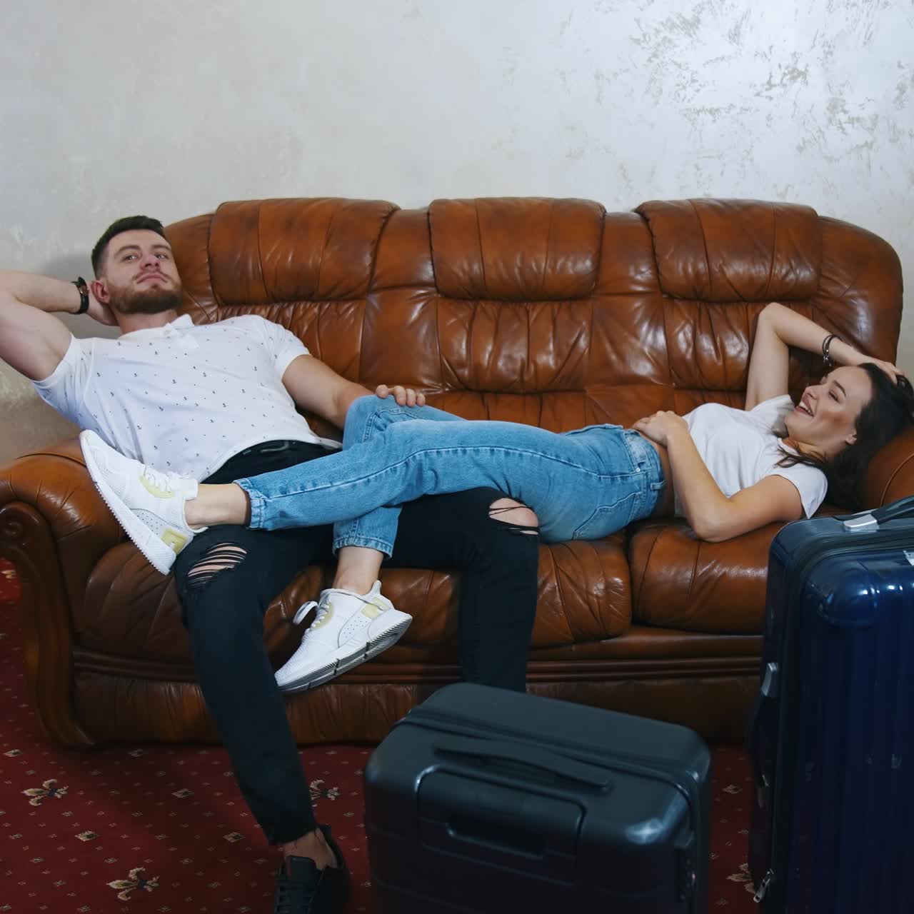 Man and woman rest on a couch tired from journey. Young couple lying on sofa waiting for the leaving the hotel on suitcases packed background
