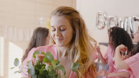 femme rousse tenant et sentant un bouquet, portant une chemise de nuit en soie rose, souriant et regardant la caméra