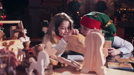 santas elf and little girl examine letters to children in a room with christmas toys