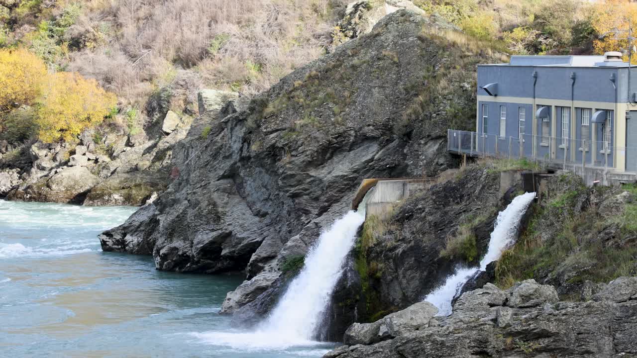 A serene view of a hydroelectric power station with cascading water in Queenstown, New Zealand. Natural landscape and industrial structure blend harmoniously