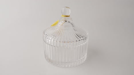 Ribbed-Carousel-Clear-Glass-Jar-In-White-Surface-Taken-By-A-Human-Hand