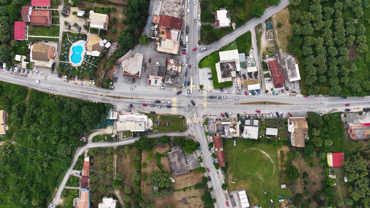 Vista aerea dall'alto con drone di un incrocio rurale con traffico di auto, case e natura verde nel villaggio di Roda, Corfù settentrionale, Grecia. Splendida prospettiva a volo d'uccello di un viaggio estivo