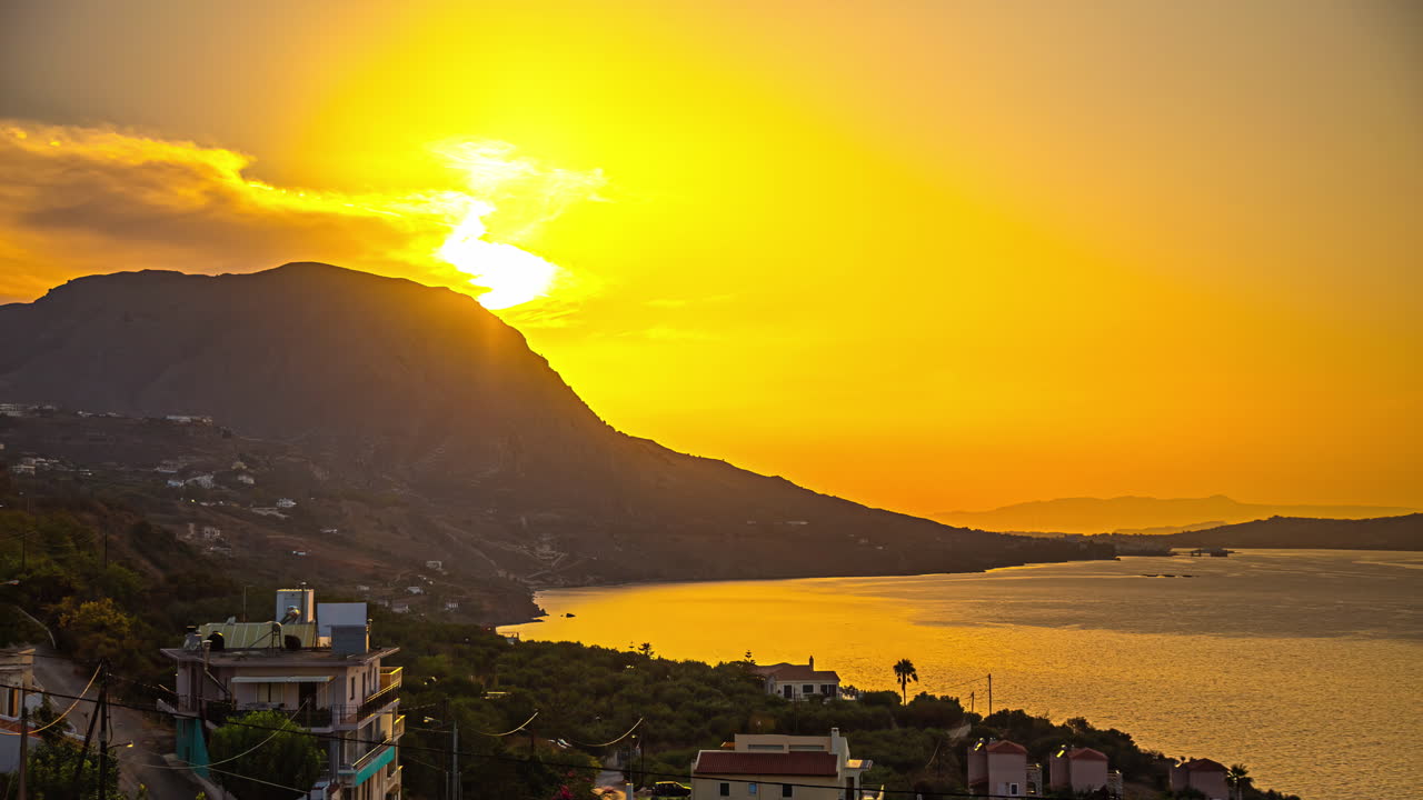 Pôr do sol dourado sobre a baía de Kalami na Grécia com silhueta da montanha
