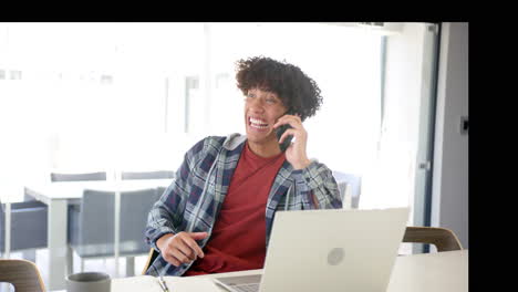 un joven biracial está usando una computadora portátil y hablando por teléfono en casa en la cocina