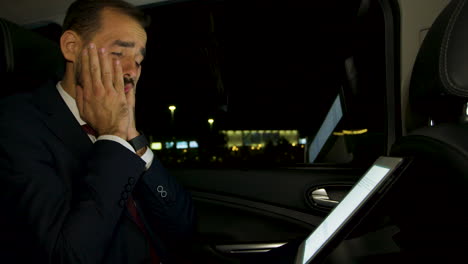 hombre de negocios trabajando por la noche en su portátil desde el asiento trasero de su coche de lujo