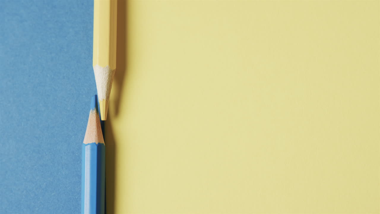 primer plano de lápices de colores amarillos y azules con espacio de copia en fondo azul y amarillo, en cámara lenta