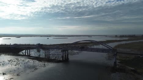 Puente-De-Carretera-Coche-Río-Desbordamiento-Inundación-Pradera-Día-Soleado-Antena-Boom-Dolly