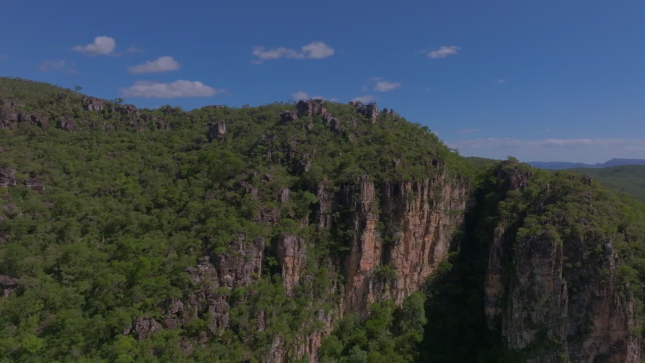 Aerial view capturing Cachoeira dos Saltos in Goiás, Brazil, with lush vegetation enveloping rocky cliffs and canyons beneath a vibrant blue sky filled with clouds