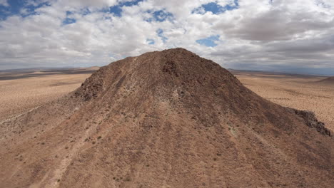 Volando-Hasta-La-Cima-De-Una-Colina-Solitaria-En-El-Paisaje-Del-Desierto-De-Mojave-Y-Luego-Bajando-La-Pendiente-Mientras-Los-Buitres-Toman-El-Cielo