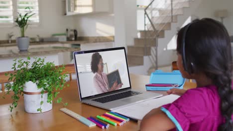 Mixed-race-girl-sitting-at-desk-using-laptop-having-online-school-lesson