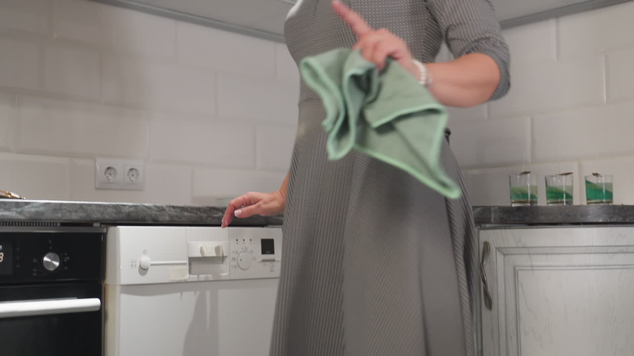 Upward view of grandmother dancing with joy in kitchen, swinging gown and hand towel in rhythm as she grooves to music, full of life and energy near oven, counter, and wooden cabinetry