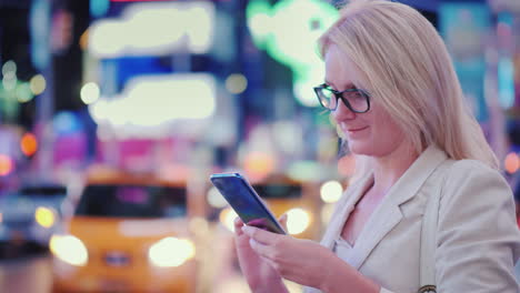 mujer de negocios usa un teléfono inteligente en la concurrida times square en nueva york están pasando los famosos taxis amarillos