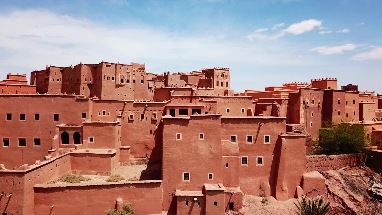 Vista dettagliata di imponenti mura di adobe di una kasbah marocchina a Ouarzazate, che evidenzia finestre geometriche e texture desertiche. Ideale per architettura, patrimonio culturale e sfondi cinematografici.