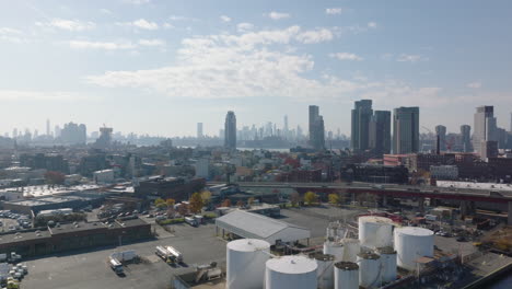 Aerial-shot-industrial-zone-with-large-tanks,-elevated-multilane-highway-and-apartment-buildings.-Skyline-with-skyscrapers-in-distance.-Brooklyn,-New-York-City,-USA