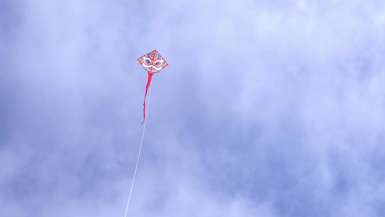 Bright Red and White Kite With Face Design Flying High in Cloudy Sky