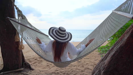 Mujer-Asiática-Sentada-Y-Columpiándose-En-Una-Hamaca-En-Una-Playa-Tropical-En-El-Paisaje-Marino-De-Tailandia-En-La-Vista-Trasera-De-Cámara-Lenta-De-Fondo