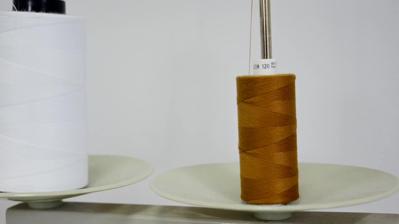 Two large thread cones, one white and one mustard yellow, sit on a metal thread stand beside an industrial sewing machine