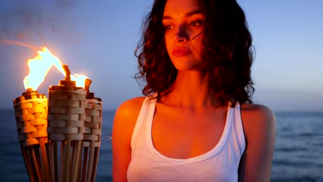 portrait female holding flaming torch, burning fire, girl with curly hair looking into camera, tropical islands, on background sea ocean