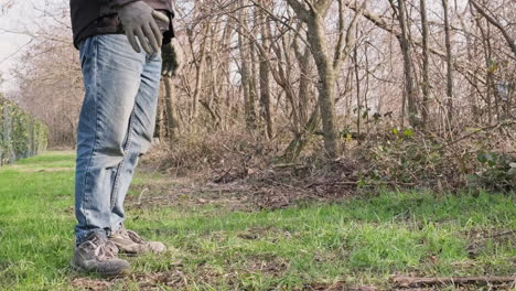 Hombre-En-Jeans-Azules-Con-Chaqueta-Negra-Y-Guantes-Parados-Frente-Al-Bosque-Durante-El-Soleado-Día-De-Invierno---Vista-Estática-De-Cerca