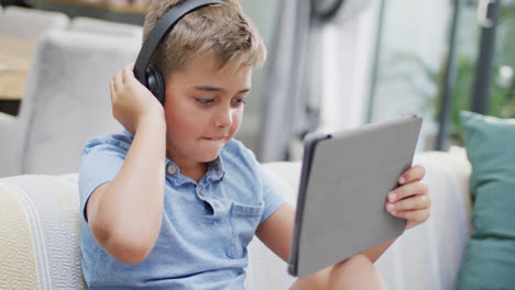 Happy-caucasian-boy-sitting-on-sofa-and-using-tablet,-slow-motion