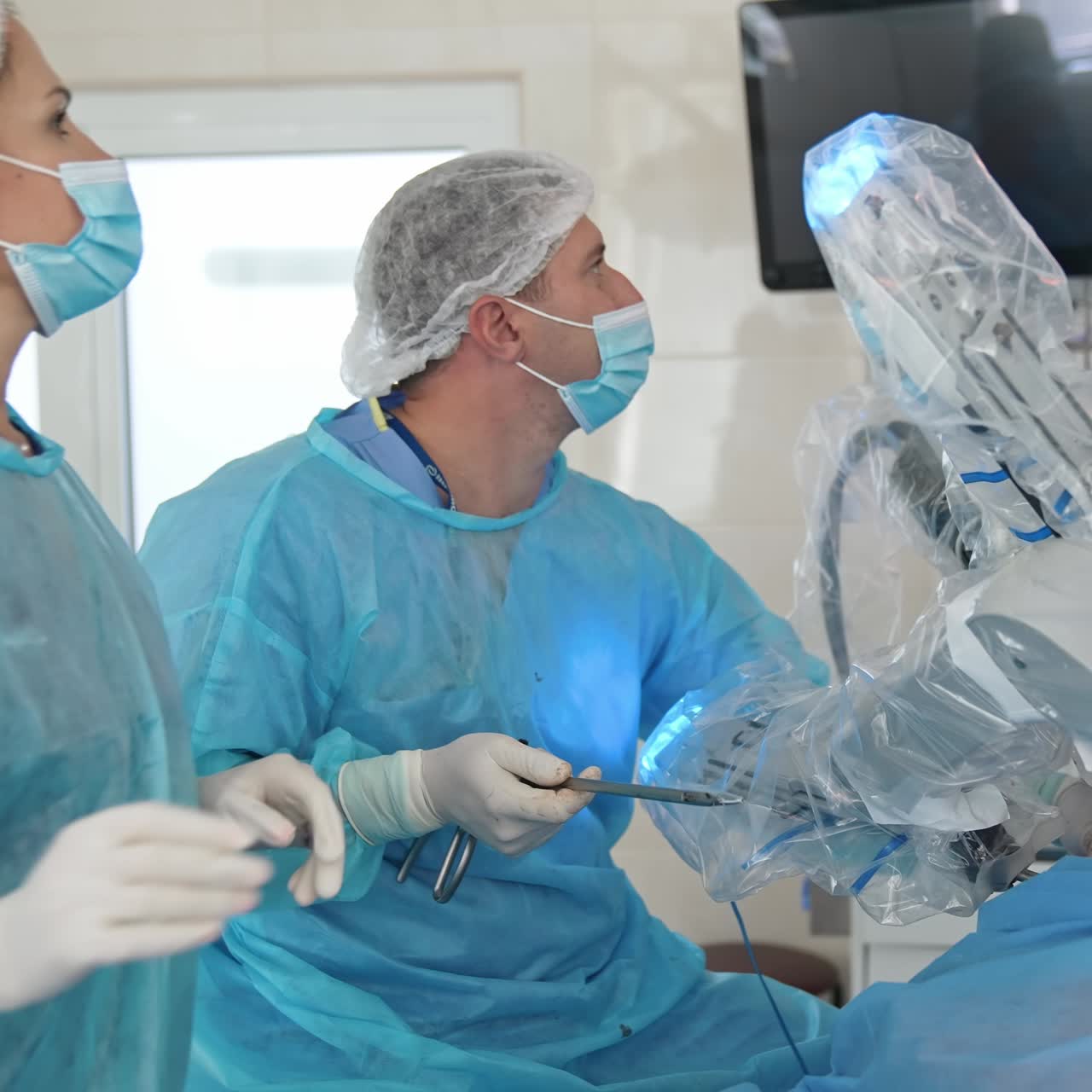 Robotic arms moving during the operation. Surgeon controls the running of operation. Male and female doctors in the operating room