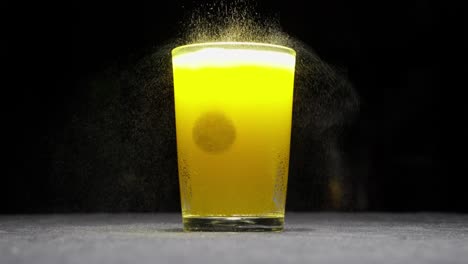 glass of effervescent fizzy orange flavor drink with vitamin tablet floating and black background