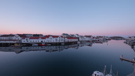 Amanecer-En-Henningsvær,-Islas-Lofoten,-Noruega,-Mostrando-El-Pueblo-Pesquero,-Casas-A-Lo-Largo-Del-Agua,-Con-Un-Cielo-Rosa-Y-Azul,-Gaviotas-Y-Agua-Tranquila-Que-Refleja-El-Cielo