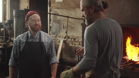 two blacksmiths shaking hands and talking in workshop