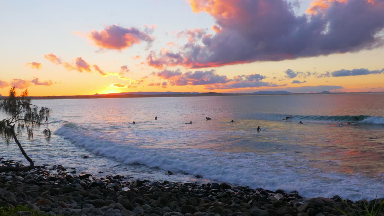 la gente monta las grandes olas durante la puesta de sol en la playa en el estado australiano de queensland