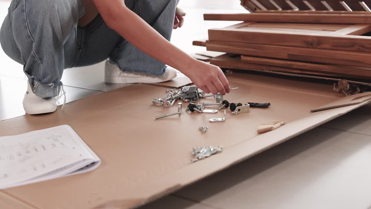 Person assembling wooden furniture using instructions and tools in a well-lit room. Focus on hands and materials