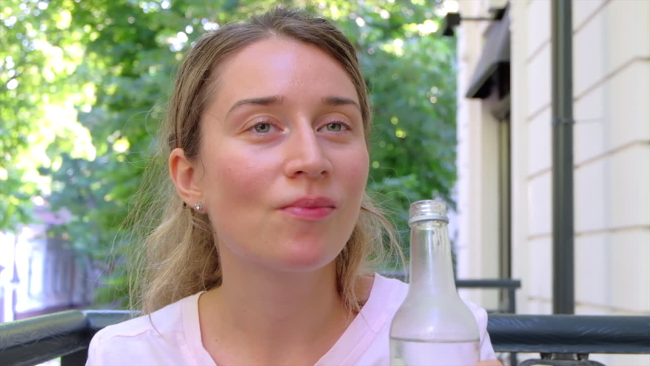 Close up of a woman drinking a bottle of water at a terrace