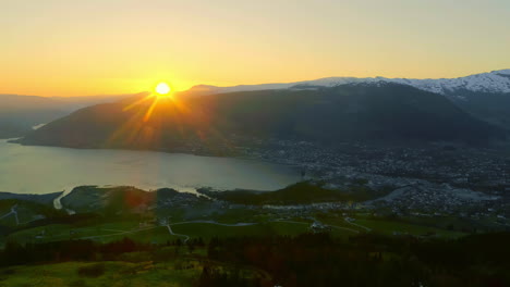 aerial drone backward moving shot over of typical norwegian village beside fjord shores in norway as sun rising from behind mountains