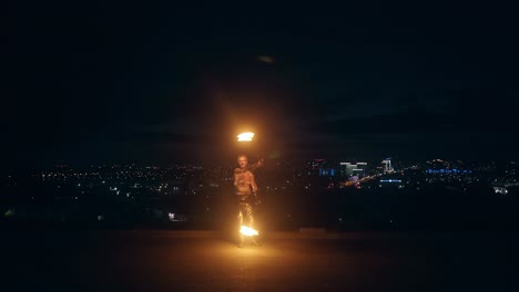 young blond male does fire dance with two torches spins torches at night on black background