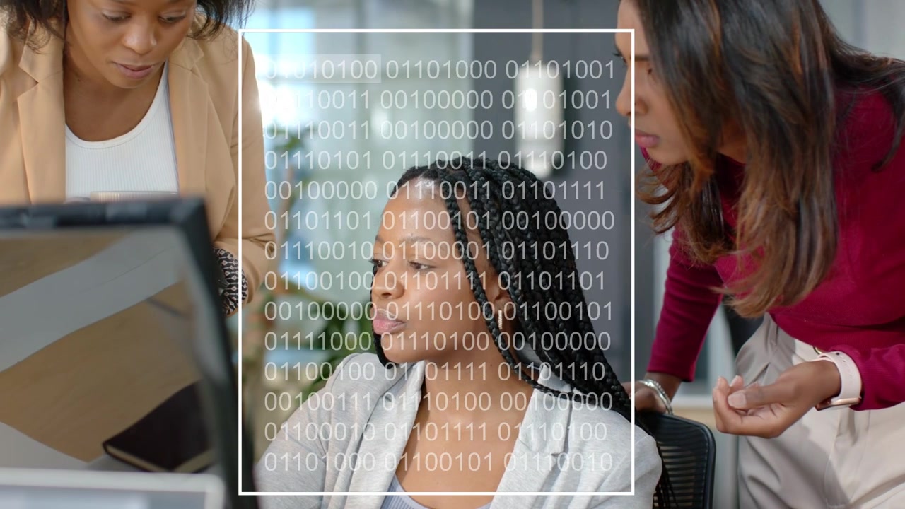 Seated woman gesturing at monitor, colleagues pointing, producing binary data overlay for review