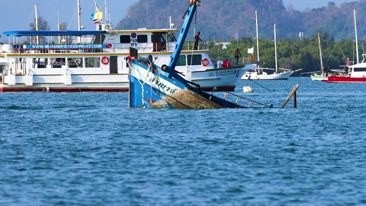 Una barca da pesca affonda gradualmente nell'oceano vicino a Phuket, Thailandia, con cieli sereni e montagne distanti