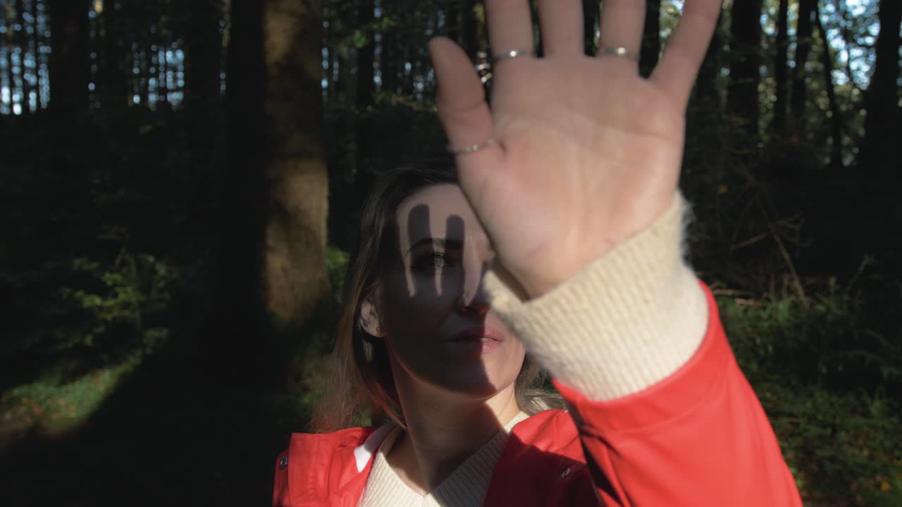 mujer sosteniendo su mano sobre la luz del sol en el bosque
