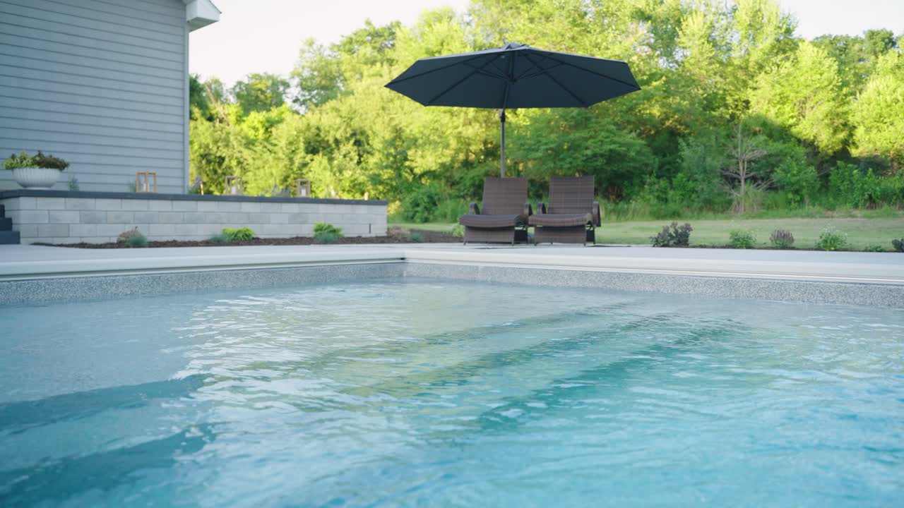 Nærbillede af neddykkede glasfiberpooltrin med liggestole og parasol.