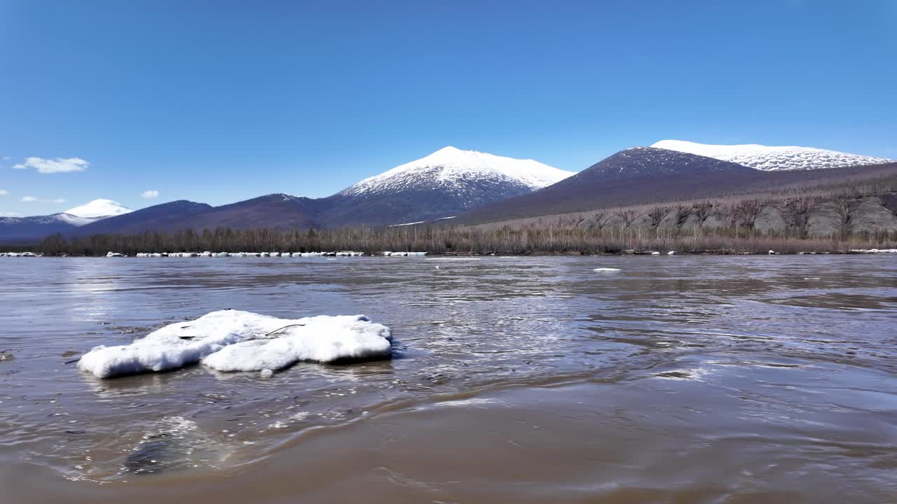 río tranquilo que fluye con montañas cubiertas de nieve en el fondo en un claro día de primavera en rusia, proporcionando un paisaje sereno y pintoresco