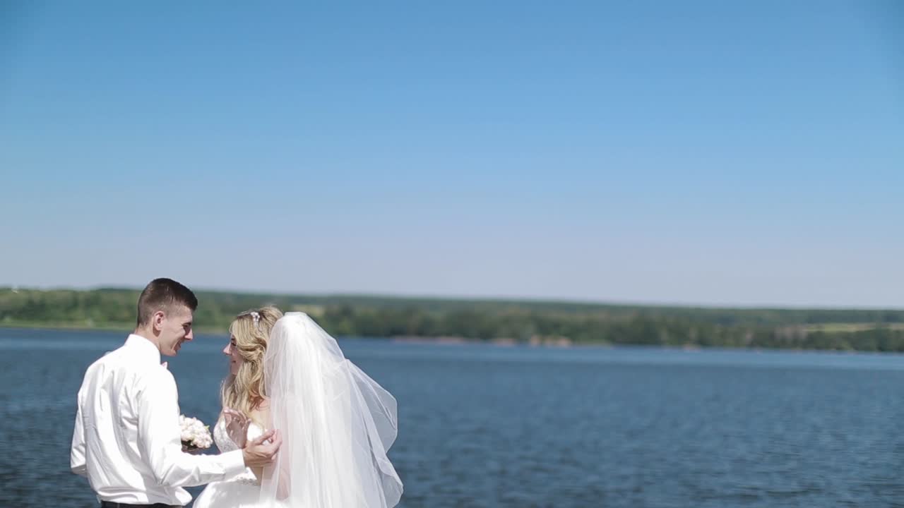 Brudepar poserer med sø i baggrunden. Brudepar, brud og gom, går og poserer på en mole.