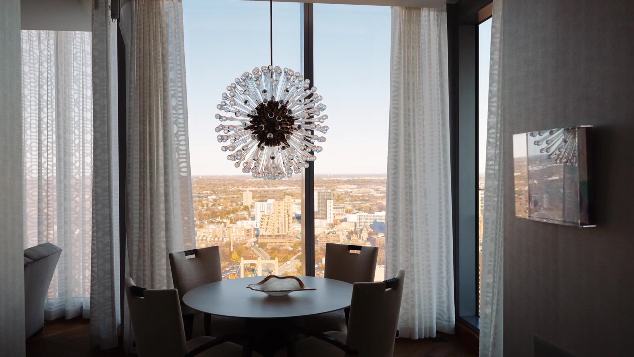 Tende che si aprono su grandi finestre in una moderna sala da pranzo con un lampadario che mostra una vista dello skyline della città