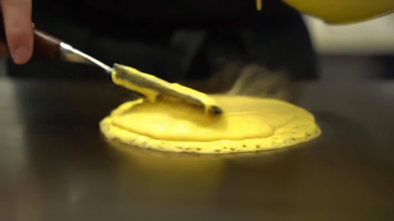Cooking Techniques: Skillfully Spreading a Yellow Batter on a Hot Surface to Create a Fluffy Culinary Delight in a Professional Kitchen Environment