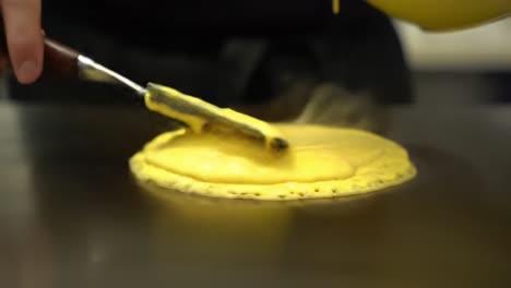 cooking techniques: skillfully spreading a yellow batter on a hot surface to create a fluffy culinary delight in a professional kitchen environment
