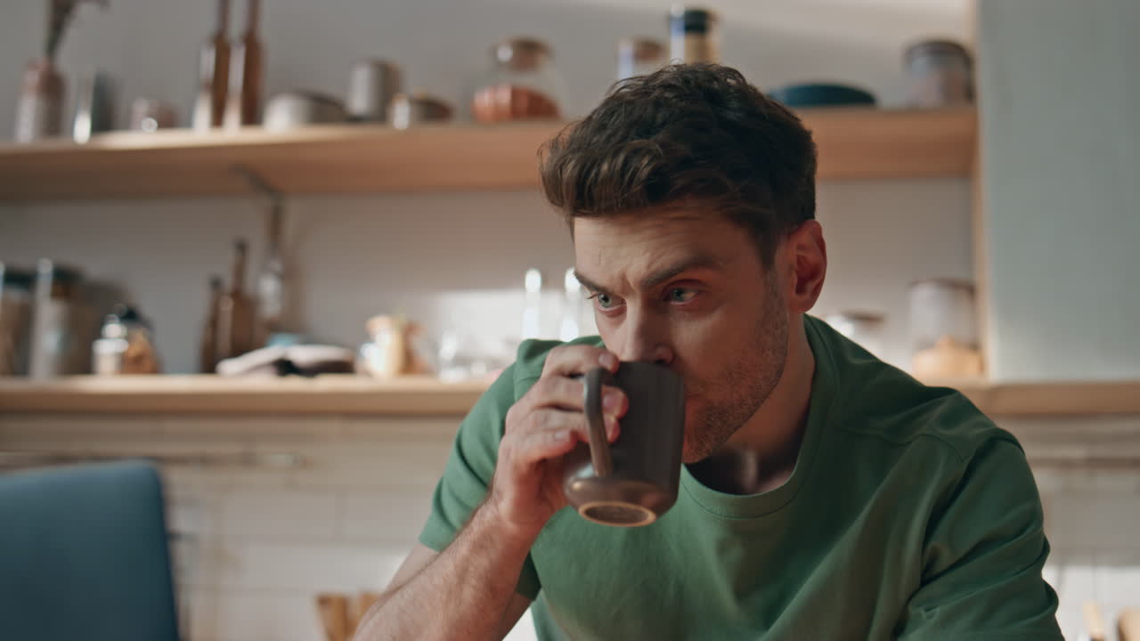 Relaxed guy sipping tea staring pc monitor at kitchen closeup. Calm man resting