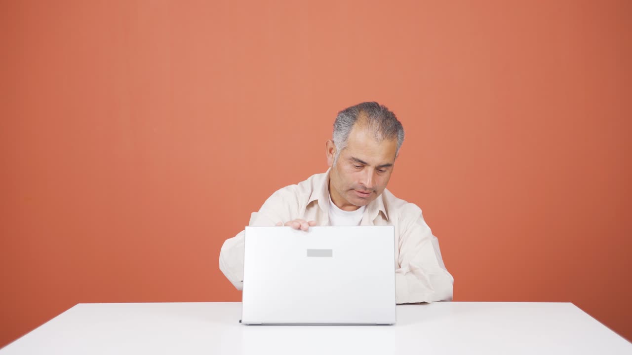 hombre cerrando la computadora portátil con expresión de enojo.