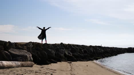 woman stands and stretches on rocky pier by the beach on a sunny day