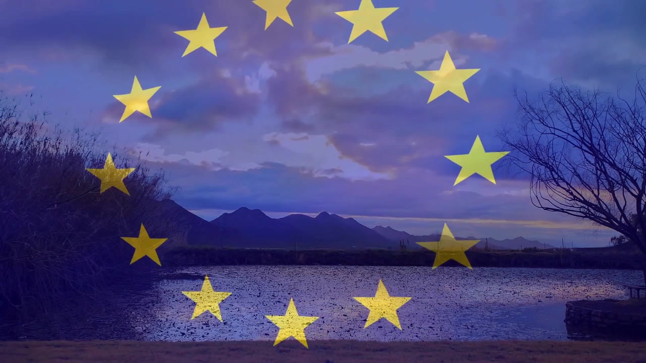 Skybevegelse starter, en gyllen EU-stjernekrets roterer idet solen kommer frem bak fjellene og lyser opp innsjøen.