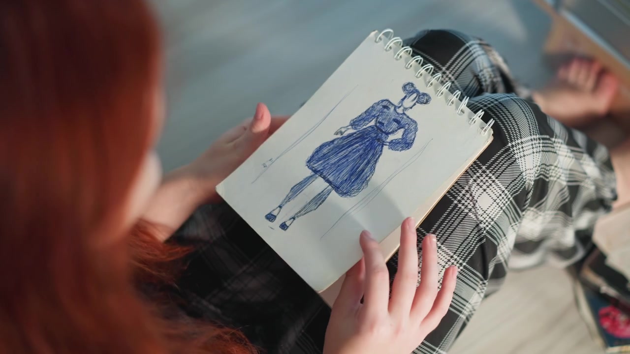 Donna dai capelli rossi tiene in grembo uno schizzo di un vestito blu, pantaloni a quadri visibili, delicate pennellate definiscono la silhouette, la postura riflessiva suggerisce uno studio di stilista o un casting di modelli, luce naturale soffusa.