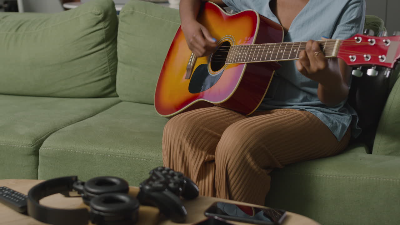 chica tocando la guitarra sentada en el sofá mientras su compañero de cuarto usa la computadora