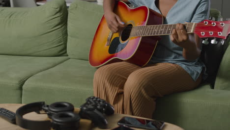 Girl-Playing-Guitar-Sitting-On-Sofa-While-Her-Male-Roommate-Using-The-Computer