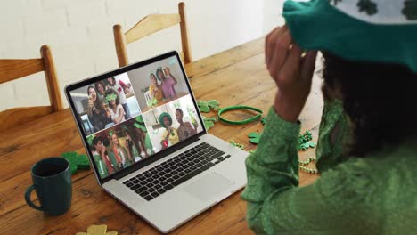 Mixed-race-woman-at-home-using-laptop-making-video-call-on-st-patrick's-day